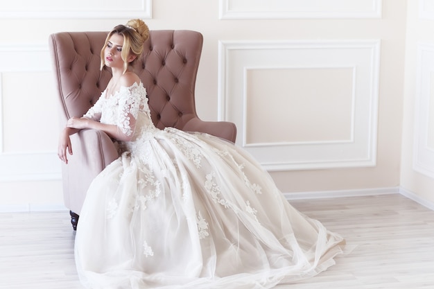 Jovem e linda noiva. Penteado de casamento, cabelo loiro, vestido de noiva, maquiagem e buquê de noiva. Tiro interno