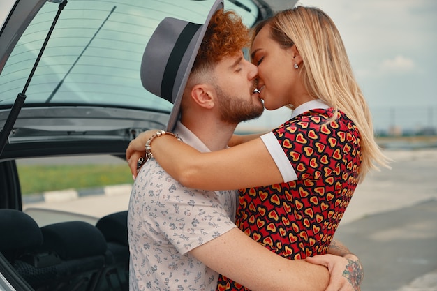 Jovem e mulher beijando na mala do carro