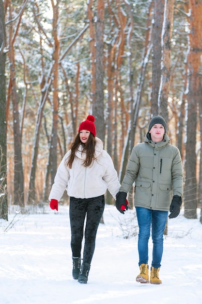 Jovem e mulher caminha no inverno pela floresta e segura as mãos Amantes caminham no parque nevado Quadro vertical