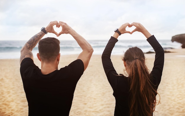 Jovem e mulher fazendo coração com as mãos assinam manhã aproveitando a pausa para treino na praia no oceano