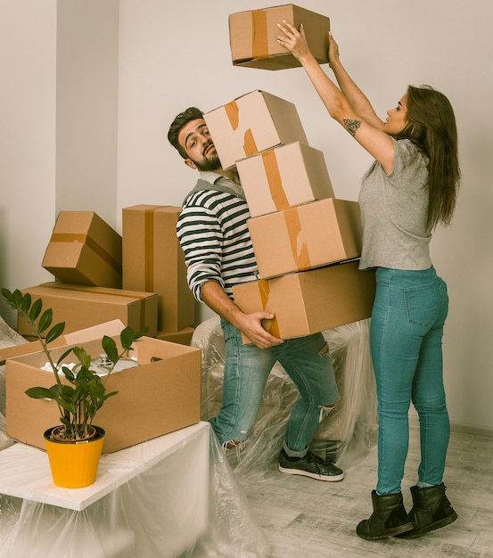 Foto jovem e mulher, movendo-se em nova casa, segurando muitas caixas de papelão.