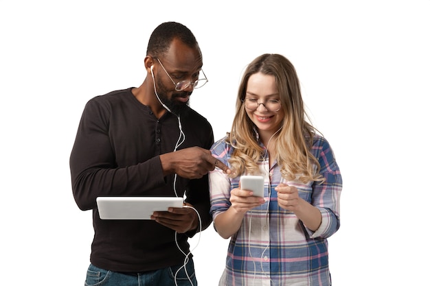 Jovem e mulher usando laptop, dispositivos, gadgets isolados no fundo branco do estúdio.