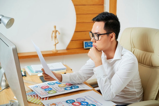 Jovem e pensativo designer de ux lendo documento com especificação de requisitos para novo projeto