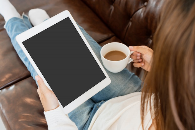 Jovem é relaxante no sofá confortável e usando o tablet em casa.