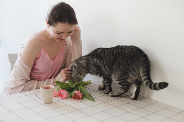 Jovem e seu gato cheirando tulipas cor de rosa frescas pela manhã em casa