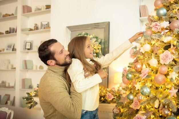 Jovem e sua filha decorando uma árvore de Natal