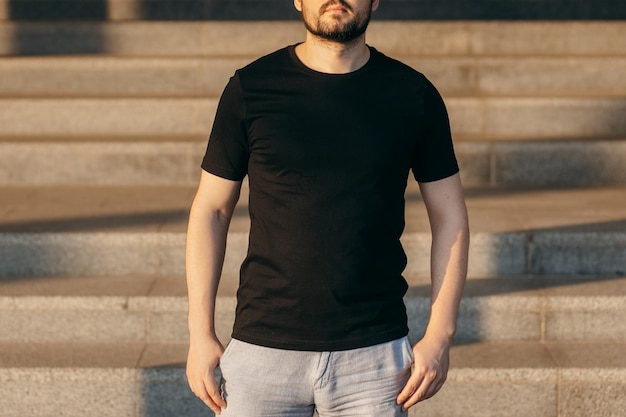 Jovem elegante barbudo em uma camiseta preta e óculos de sol Foto da rua