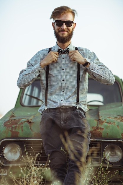 Jovem elegante bonito vestindo camisa e gravata borboleta com carros antigos