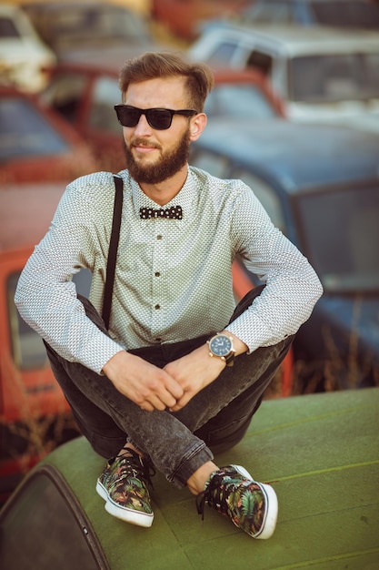 Jovem elegante bonito vestindo camisa e gravata borboleta no campo de carros antigos