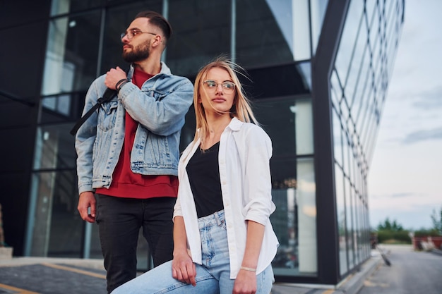 Jovem elegante com mulher em roupas casuais ao ar livre juntos perto de construção de negócios Concepção de amizade ou relacionamentos