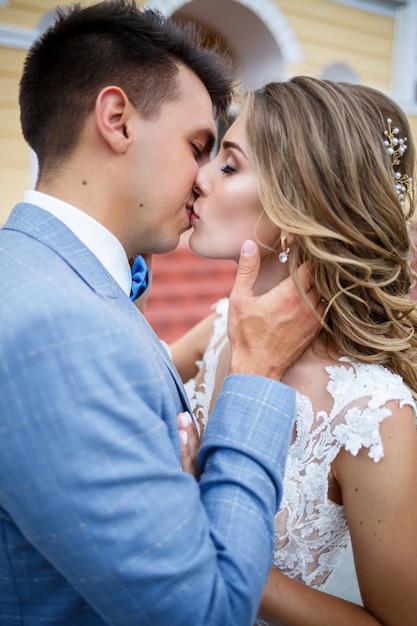 Jovem elegante com o traje do noivo e da noiva linda garota em um vestido branco com um trem andando no fundo de uma grande casa com colunas no dia do casamento