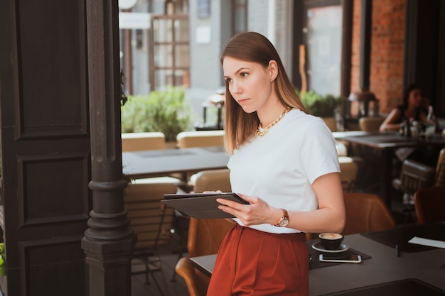 Jovem elegante com tablet digital trabalhando em um café de rua