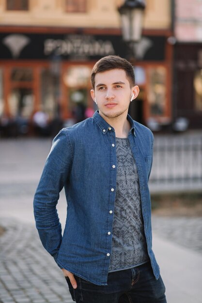 Jovem elegante em camisa jeans azul com fones de ouvido sem fio Homem ouvindo música