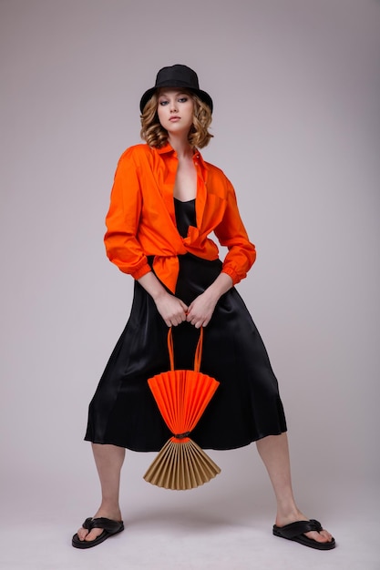 jovem elegante em uma bolsa de camisa laranja de chapéu preto posando em fundo branco