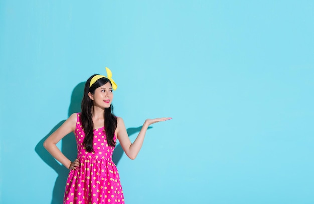 jovem elegante fazendo apresentação posando apresentando área vazia e de pé em fundo azul com roupas de vestido bonito de verão.