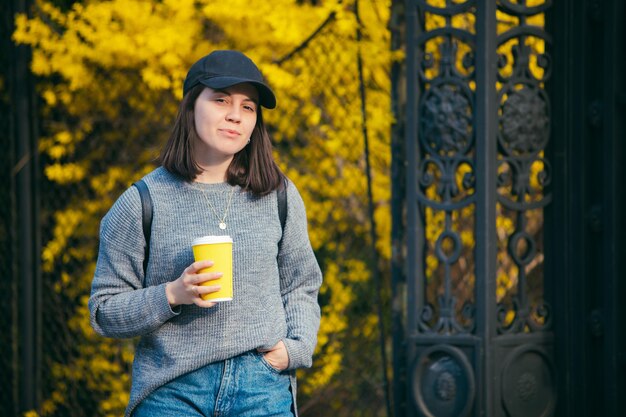 Jovem elegante no boné bebendo café ao ar livre do copo de papel amarelo