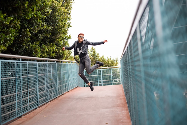 Jovem elegante vestindo menino pulando em uma ponte