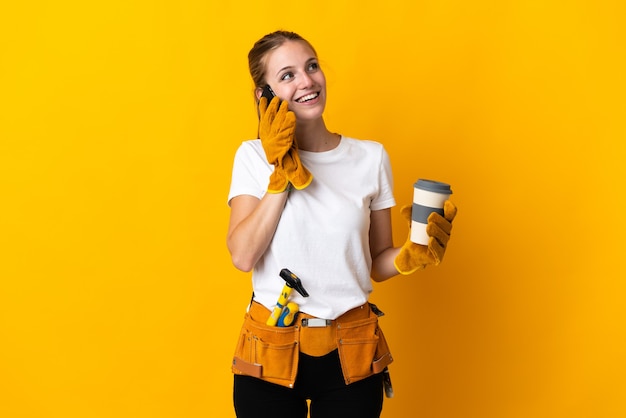 Jovem eletricista isolada em amarelo segurando café para levar e um celular