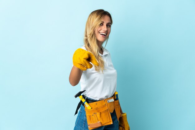 Jovem eletricista loira isolada apontando para a frente com uma expressão feliz