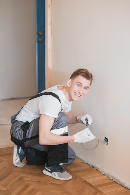 Jovem eletricista sorridente, instalando o soquete elétrico na parede da casa