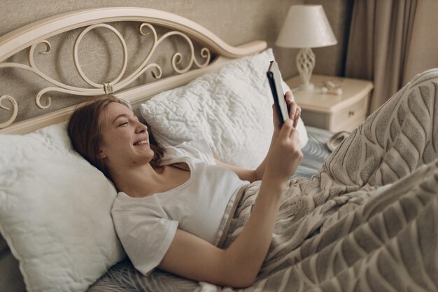 Jovem em casa, deitada na cama no quarto com tablet digital