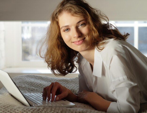 Jovem em casa na cama usando laptop