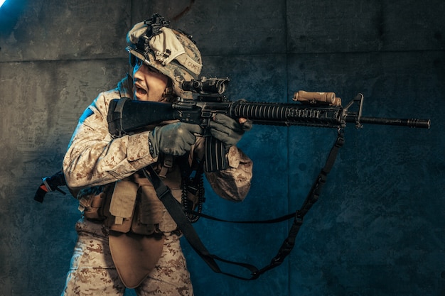 Jovem em equipamento militar, um soldado mercenário nos tempos modernos, em uma parede escura no estúdio