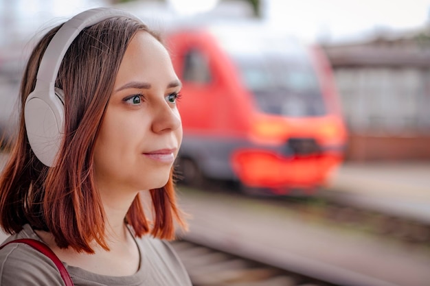 Jovem em fones de ouvido sem fio fica na plataforma esperando o trem Retrato de passageira ouvindo música no fundo do trem embaçado