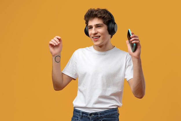 Jovem em fones de ouvido usando celular enquanto ouve música sobre fundo amarelo