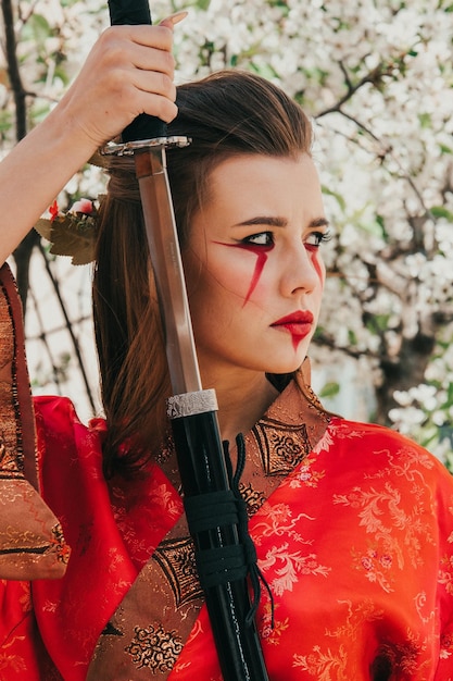 Jovem em kimano tradicional em um jardim florido com katana de espada japonesa samurai na imagem de uma mulher guerreira