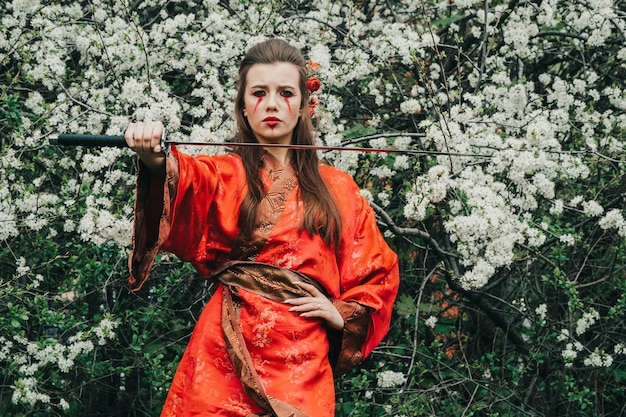 Jovem em kimano tradicional em um jardim florido com katana de espada japonesa samurai na imagem de uma mulher guerreira