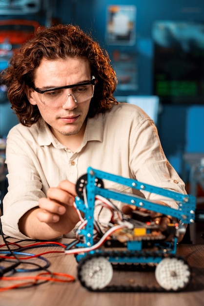 Foto jovem em óculos de proteção fazendo experimentos em robótica em um laboratório usando ferramentas especiais