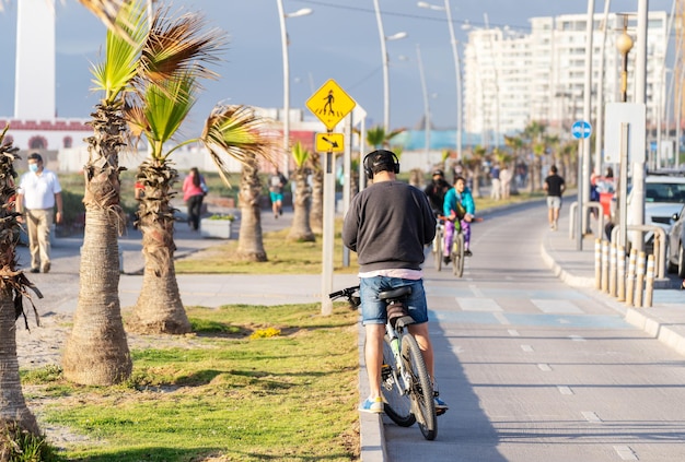 jovem em pé com uma bicicleta olhando para um celular ou dispositivo móvel com fones de ouvido em uma ciclovia