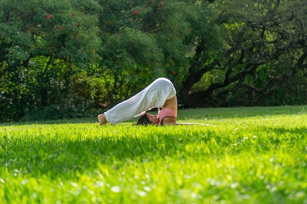 Jovem em pose de arado praticando ioga em um conceito verde ParkWellness