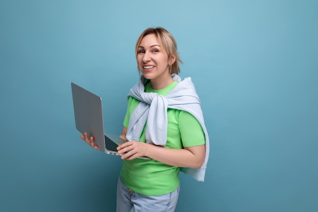 Jovem em roupa casual fica com confiança segurando um laptop em suas mãos em um fundo azul