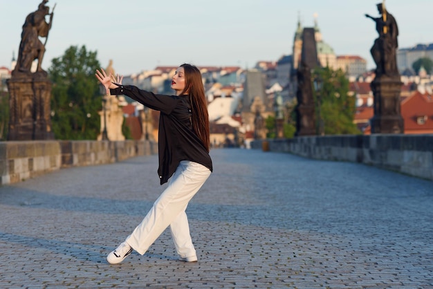 Jovem em roupas casuais elegantes dançando na ponte de pedra da cidade velha em praga ativa