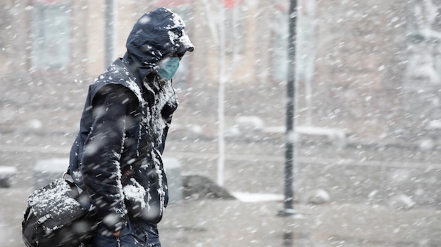 Jovem em roupas escuras e médico para proteger contra a máscara COVID-19 se move na rua com neve