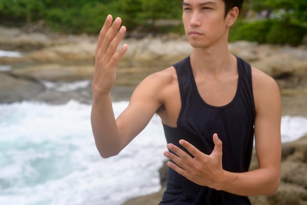 Jovem em roupas esportivas fazendo arte marcial Qigong Tai chi na rocha à beira-mar