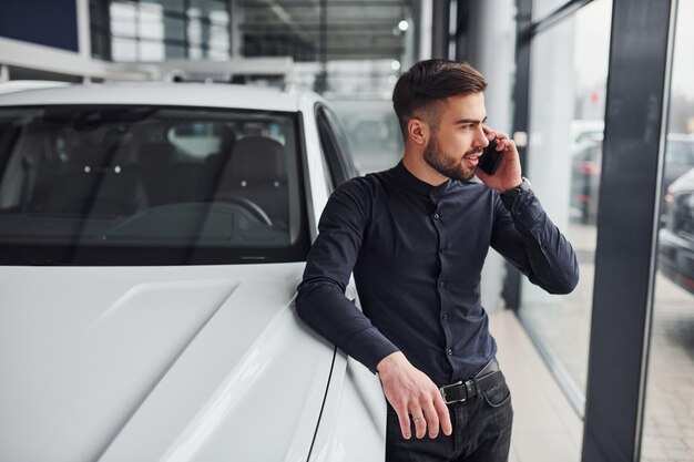 Foto jovem em roupas formais está perto de carro novo e caro.