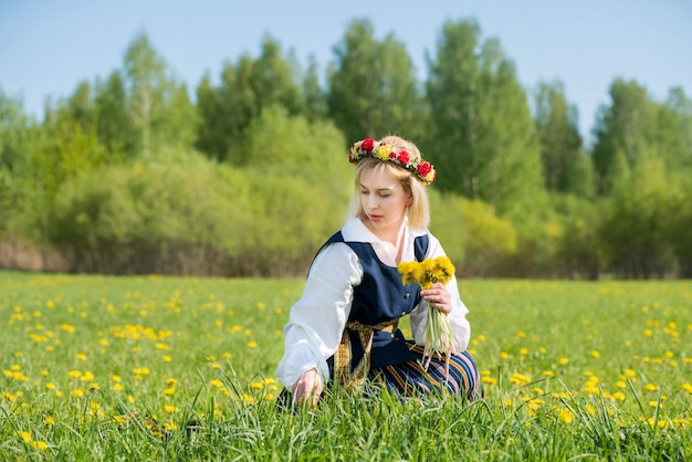 Jovem em roupas nacionais usando coroa de dente de leão amarelo na primavera campo primavera