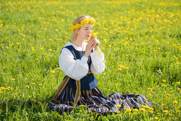 Jovem em roupas nacionais usando coroa de dente de leão amarelo no campo de primavera Primavera