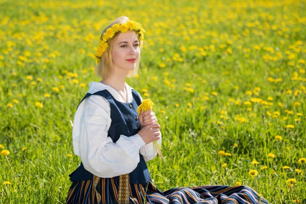 Jovem em roupas nacionais usando coroa de dente de leão amarelo no campo de primavera Primavera