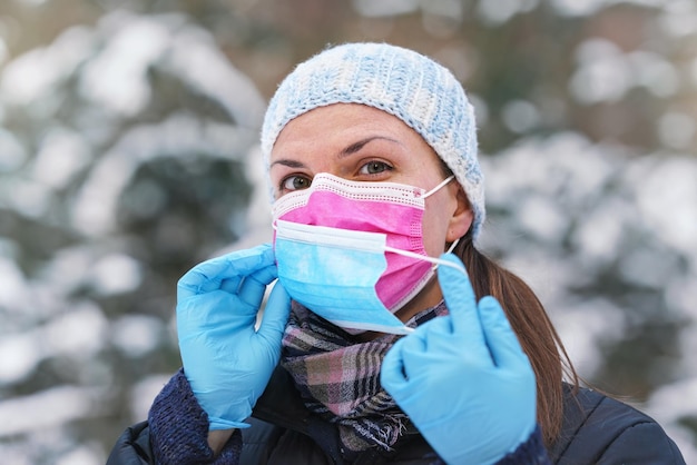 Jovem em roupas quentes de inverno usando máscara facial de vírus descartável rosa, colocando outra - alguns aconselham que duas camadas fornecem melhor proteção contra a propagação do coronavírus covid-19