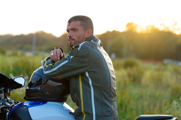 Jovem em sua motocicleta contemplando a paisagem com calma Ele está vestindo uma jaqueta de couro verde