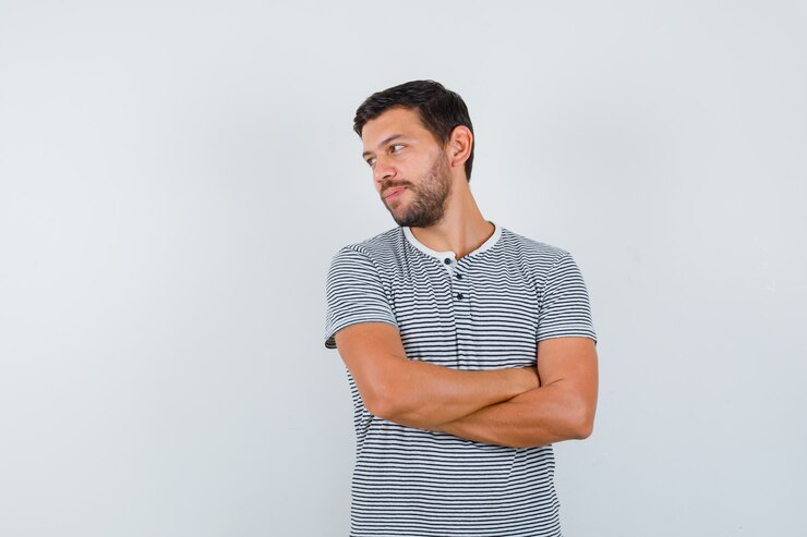Foto jovem em t-shirt, de braços cruzados, olhando para o lado e olhando com foco, vista frontal.