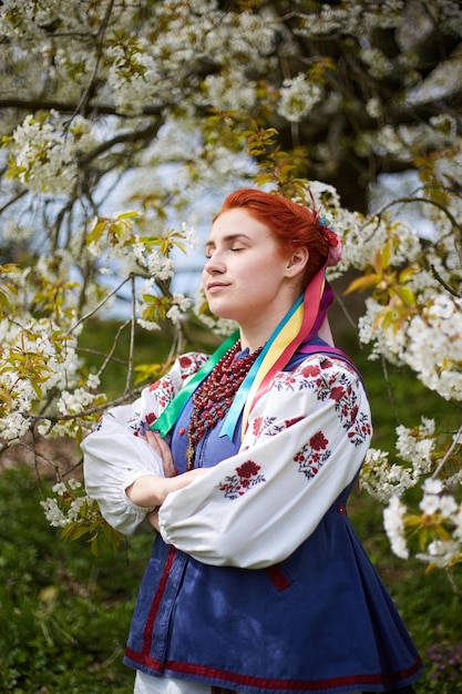 Jovem em traje nacional ucraniano Sorrindo Jovem em roupas tradicionais Fique perto da árvore florescente Paz na Ucrânia