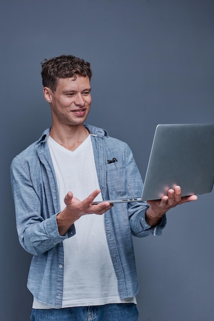 Jovem em um fundo cinzento segurando um laptop