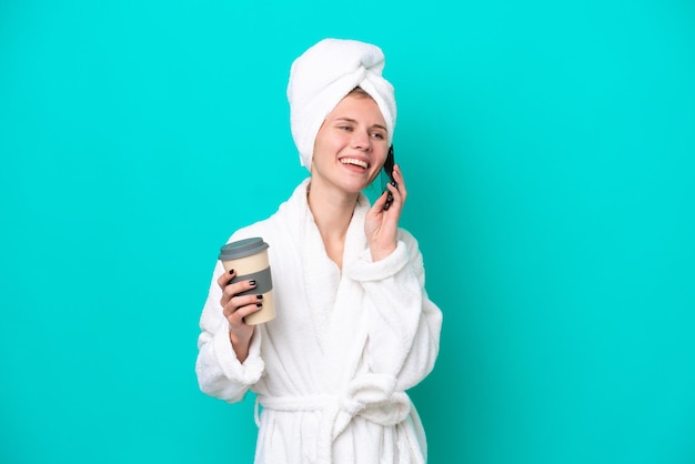 Jovem em um roupão de banho isolado em fundo azul segurando café para levar e um celular