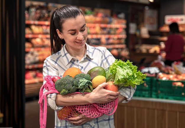 Jovem em um supermercado com legumes e frutas comprando mantimentos