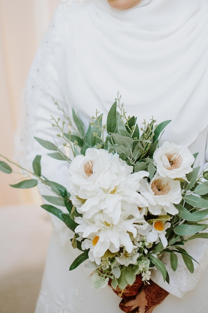 Jovem em um vestido de noiva branco tem nas mãos um buquê de flores.